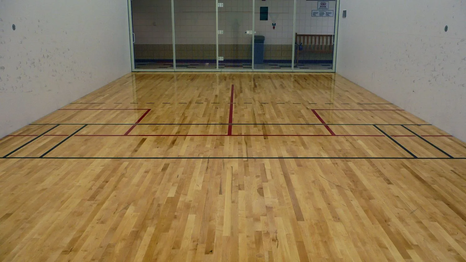 Maple racquetball court floor with red lines and a glass back wall