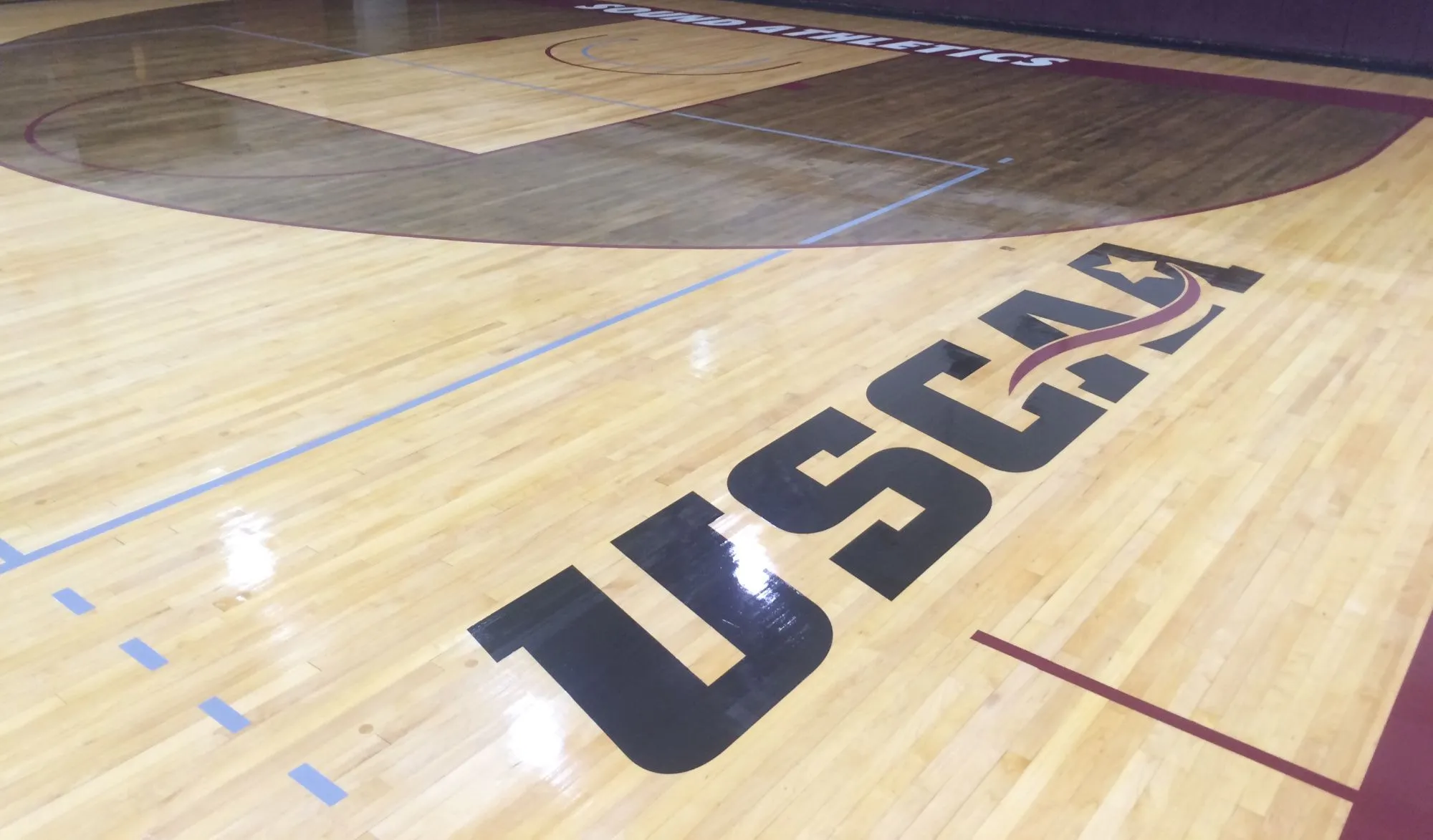 Glossy maple gym floor with large navy block lettering at center court and a maroon border