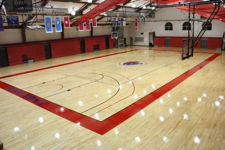 Maple gym floor with a red painted border and red wall pads in a school gym