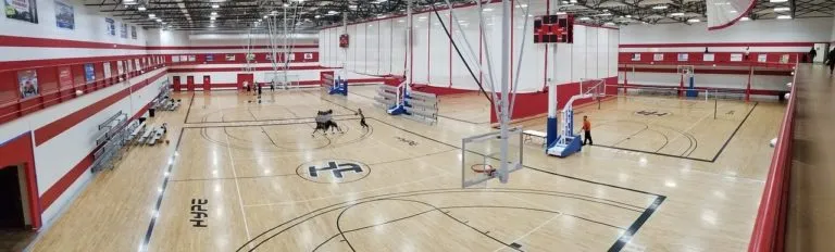 Large multi-court gym with a maple floor, red and white walls and several basketball hoops