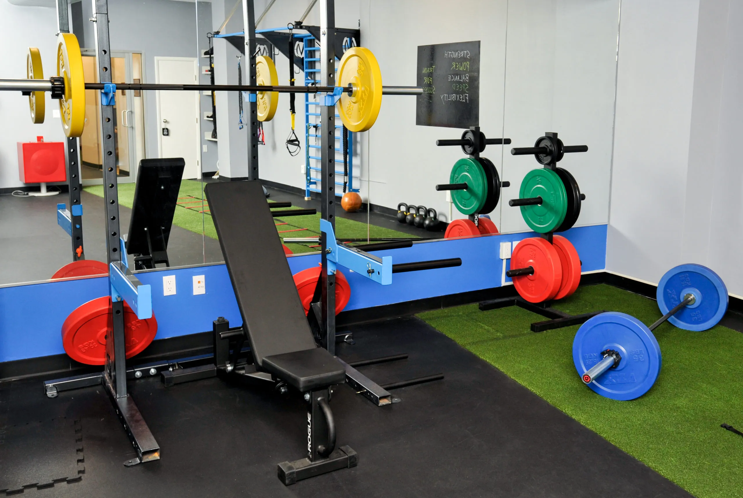 Athletic performance center weight room with rubber flooring under squat racks and benches