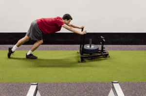 Athlete pushing a sled on an indoor turf strip in a gym