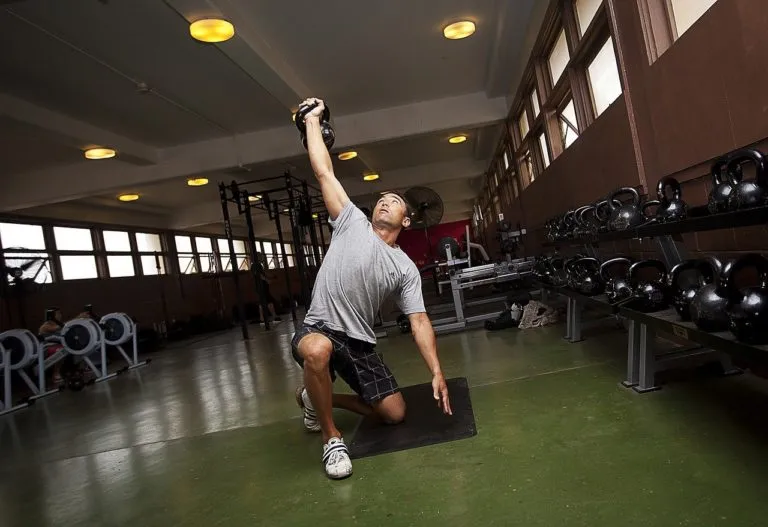 Man exercising with a kettlebell on a rubber mat in a weight room