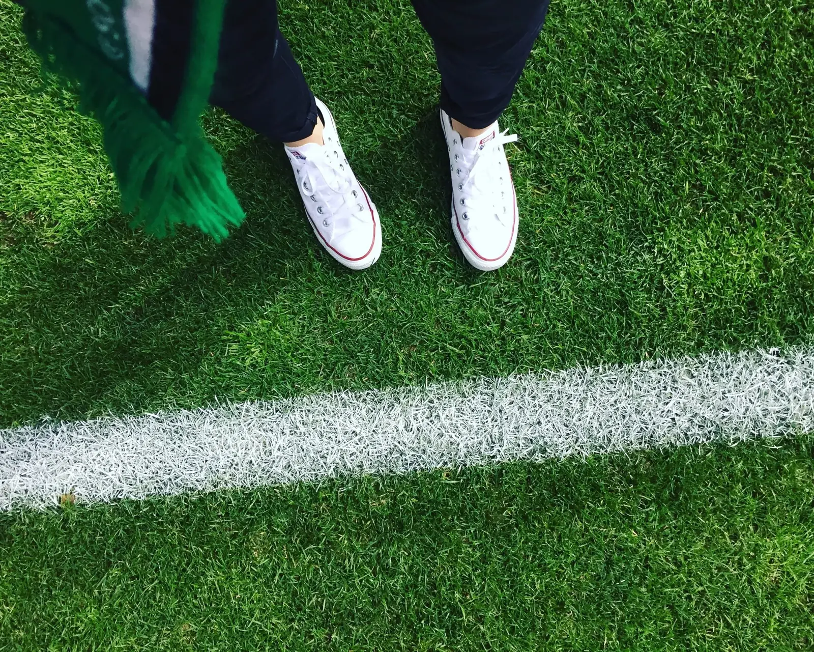 Close-up of sneakers standing on green artificial turf next to a white line