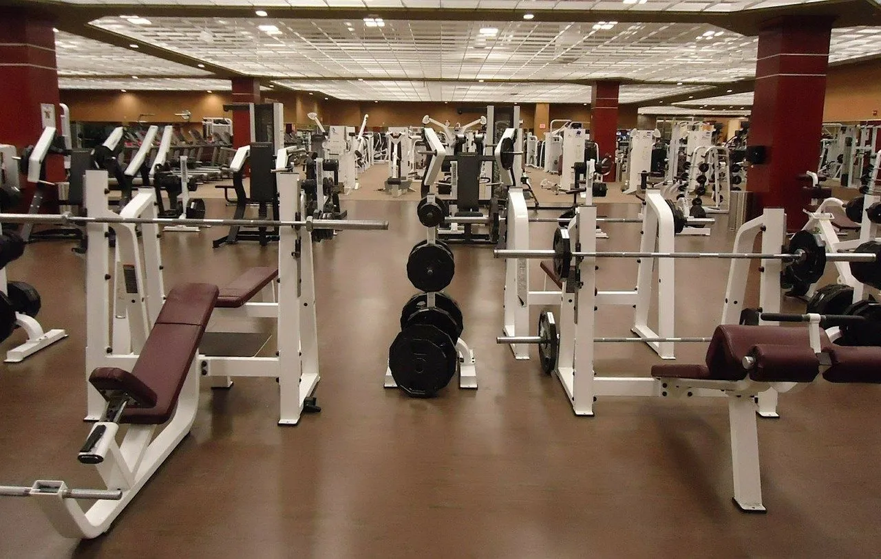Commercial gym with rows of weight machines and benches on a rubber floor