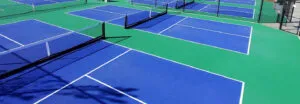 Outdoor pickleball courts with blue playing areas, green surrounds and nets