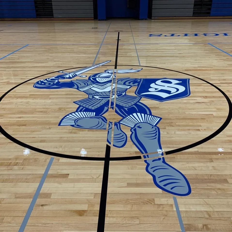 Blue knight mascot logo painted at center court on a maple gym floor