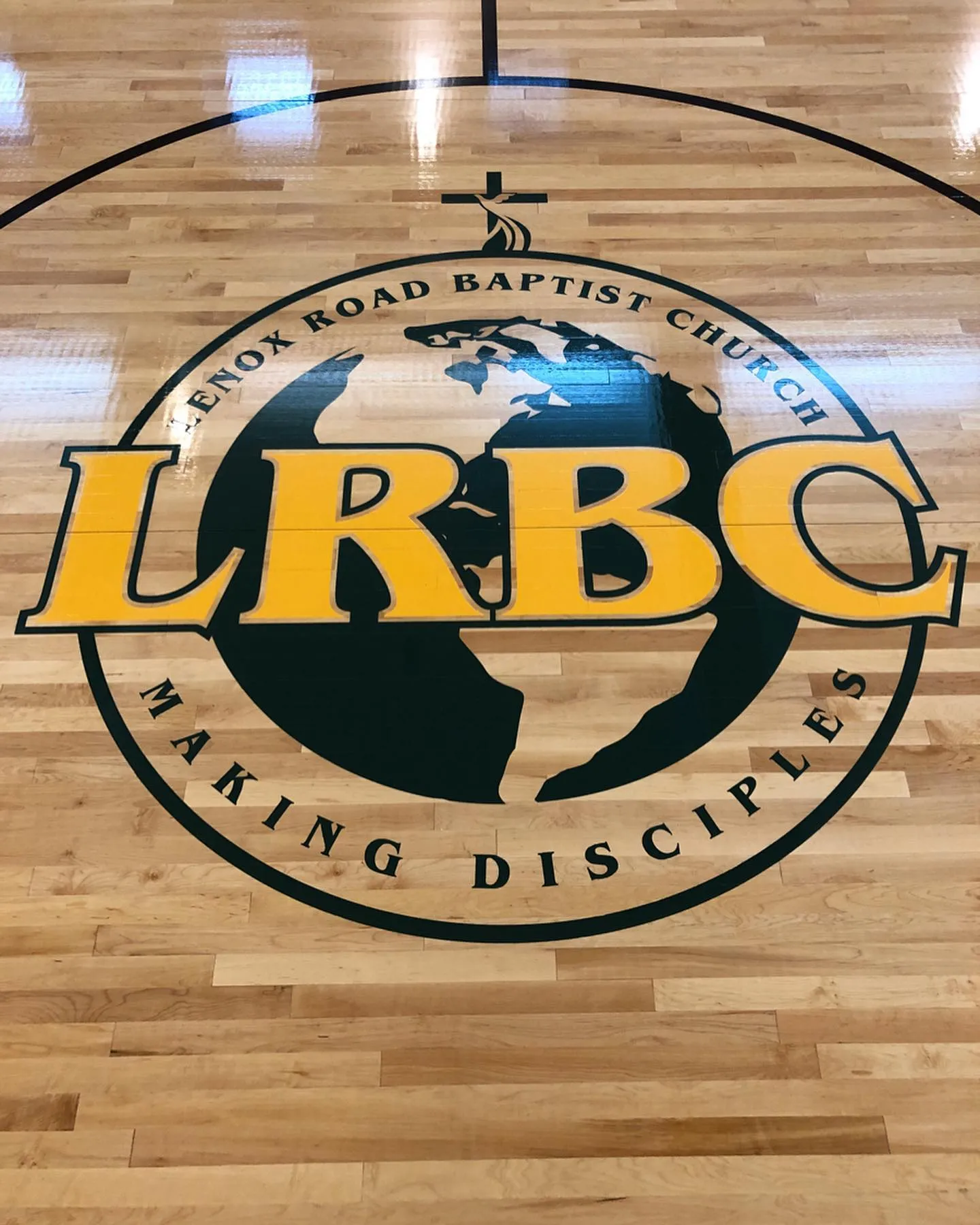 Green and gold church logo painted at center court on a maple gym floor