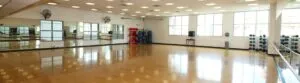 Bright aerobics room with a glossy wood floor and mirrored walls