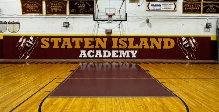 Staten Island Academy gym with a glossy maple floor, maroon key and painted wall banner