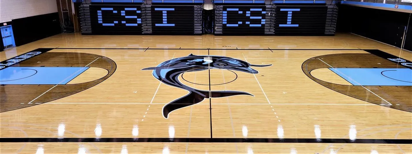 Maple gym floor with a dolphin center-court logo and light blue keys in a college gym