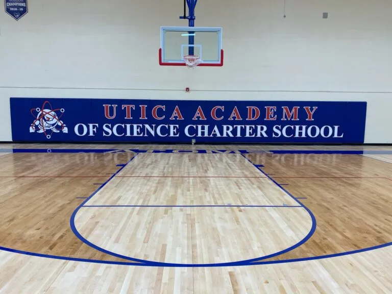 Utica Academy of Science Charter School navy wall pads above a maple gym floor with blue lines