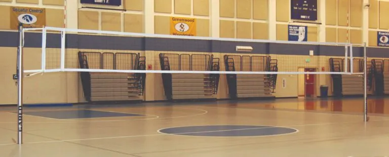Gym set up for volleyball with nets over a light-colored court