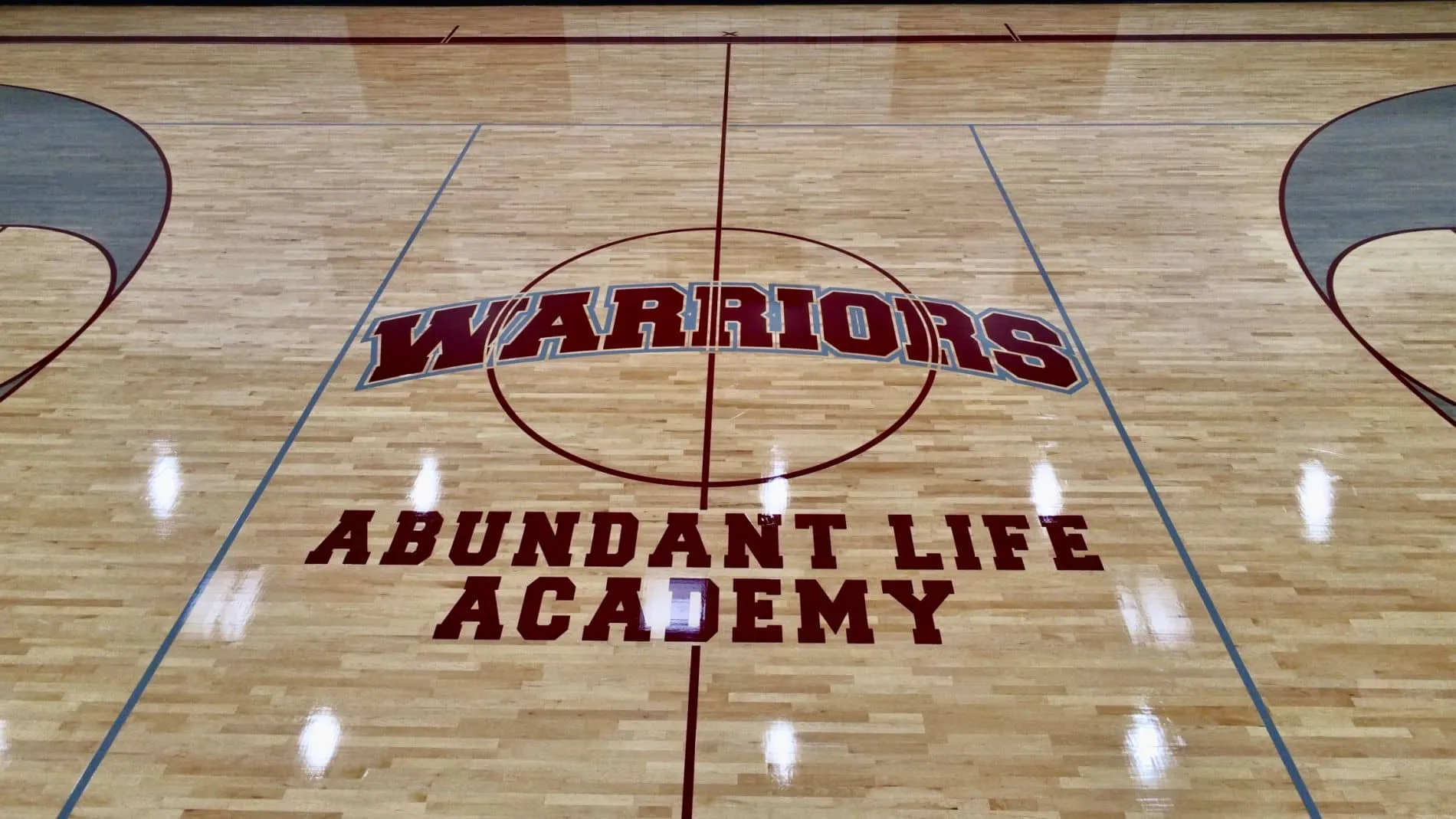 Maroon Warriors center-court lettering with a basketball logo on a refinished maple floor