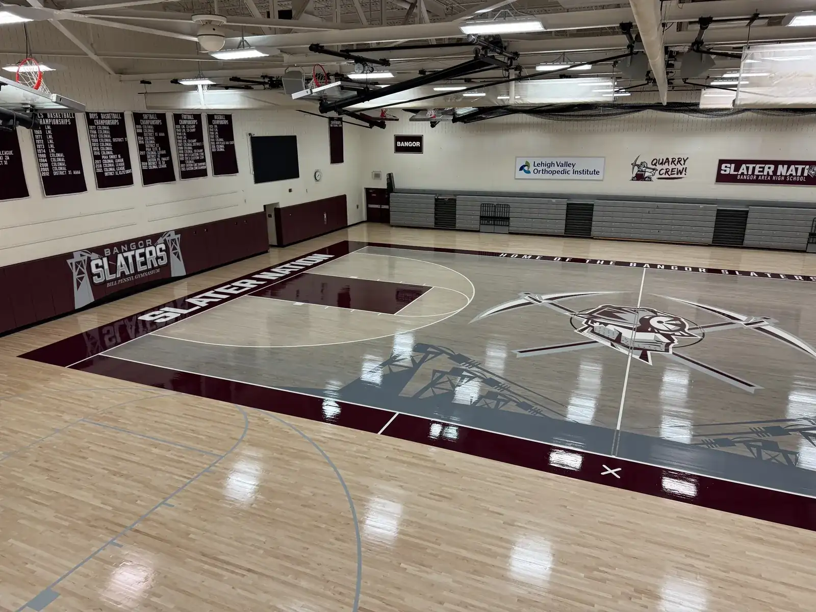 High-gloss maple gym floor at Bangor Area High School with gray stained keys, a maroon border and the SLATERS center logo