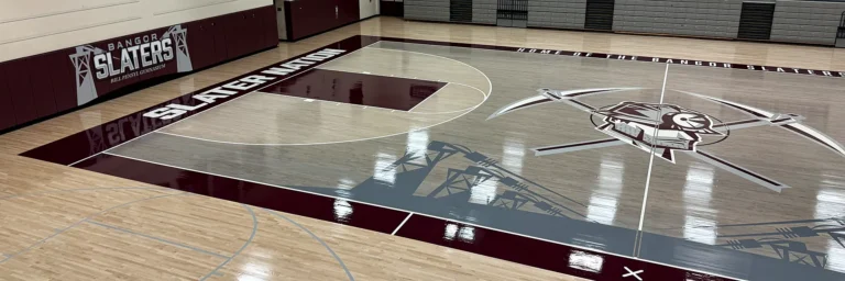 Bangor Area High School Slaters maple gym floor in Pennsylvania, seen from above: high-gloss finish, painted center-court logo and gray and maroon painted key areas and border by J and J Gym Floors