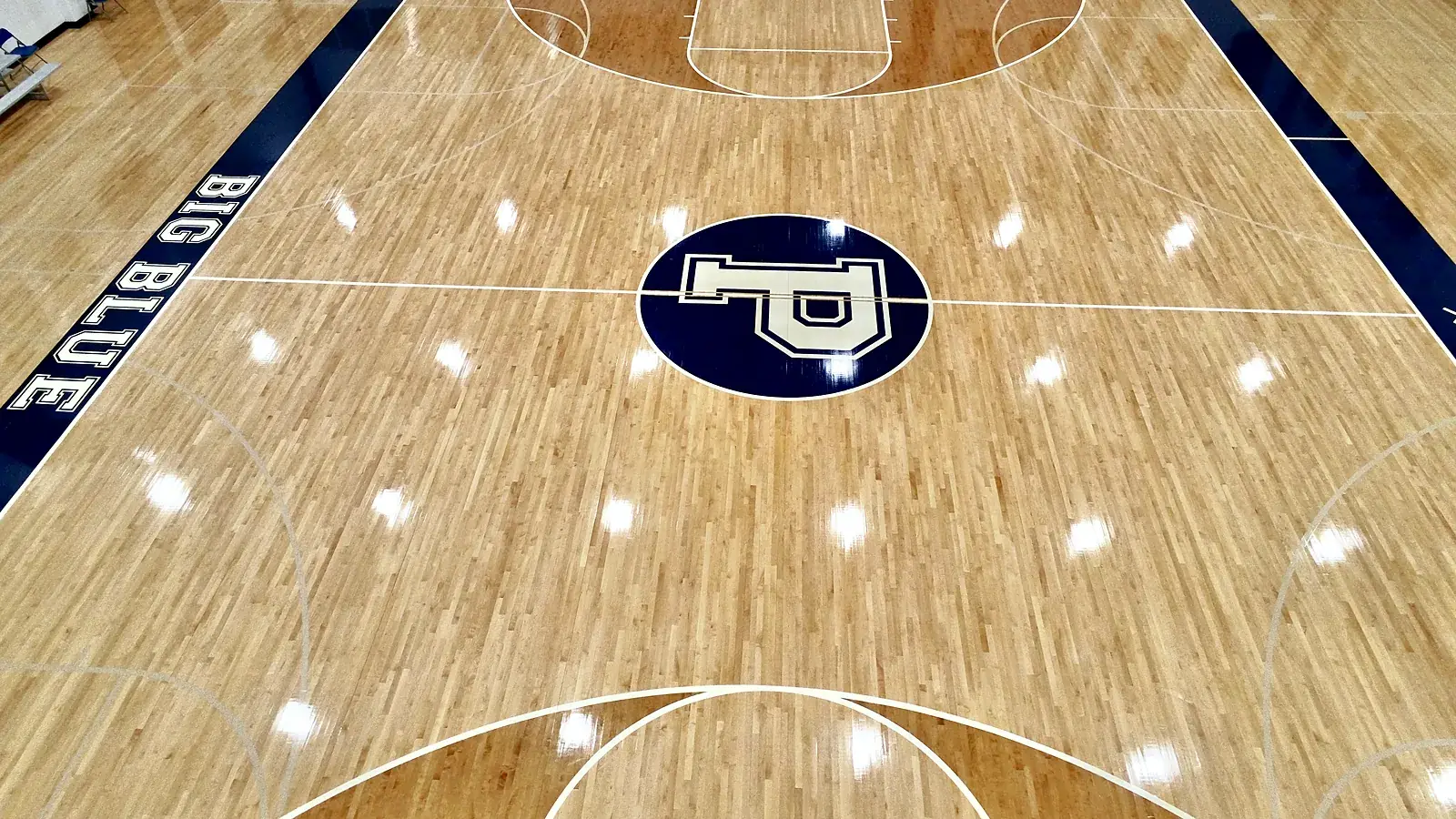 Drone view of a glossy maple gym floor with the navy P center-court logo and BIG BLUE lettering on the navy sideline border