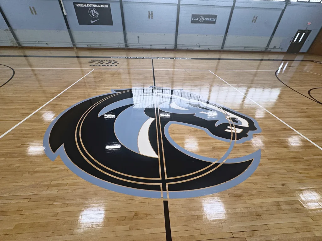 Christian Brothers Academy Colts center court logo in light blue and black on a newly refinished maple gym floor by J and J Gym Floors