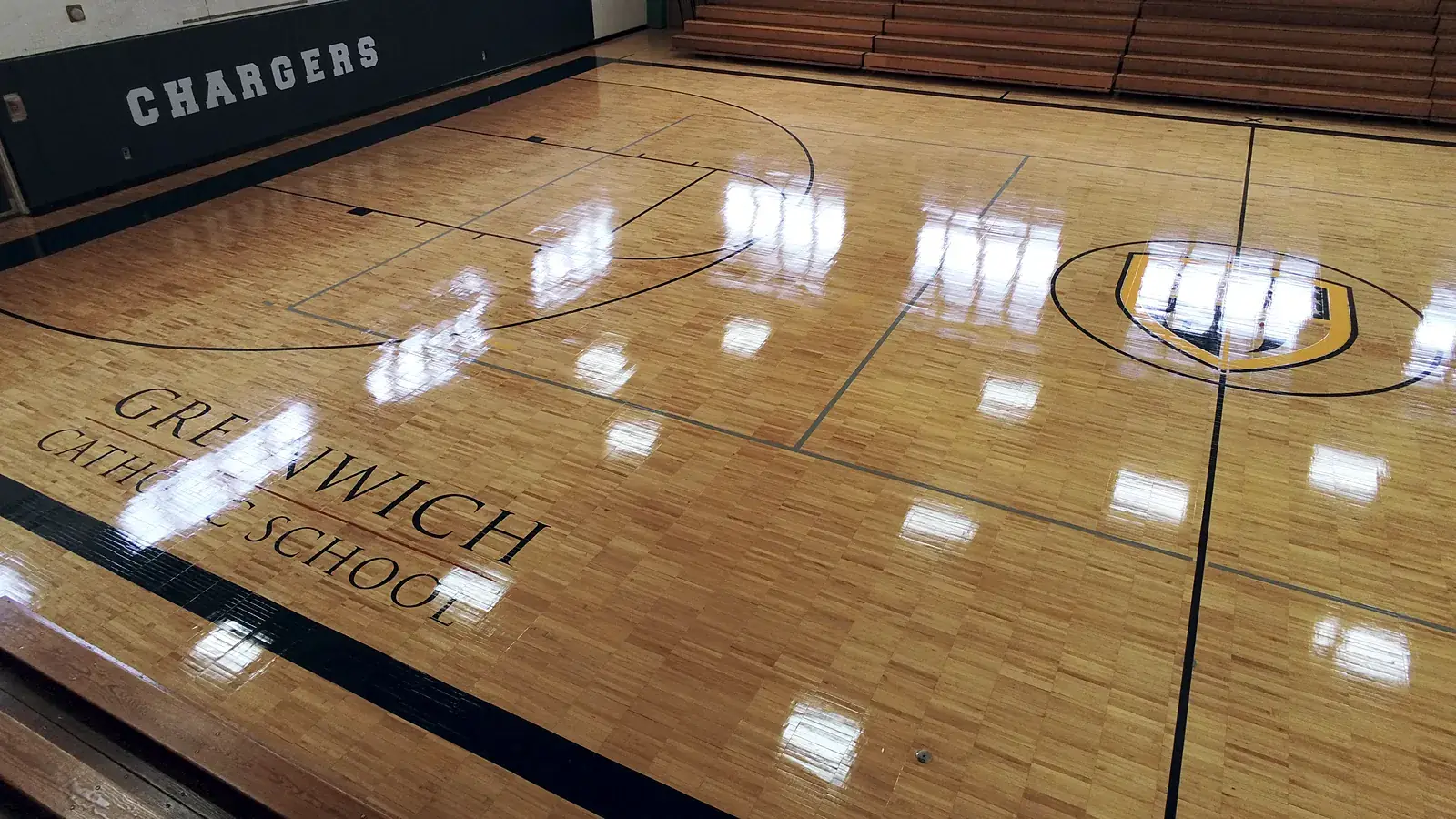 Drone view of the Greenwich Catholic School Chargers gym: high-gloss maple floor with the school crest at center court and GREENWICH CATHOLIC SCHOOL lettering