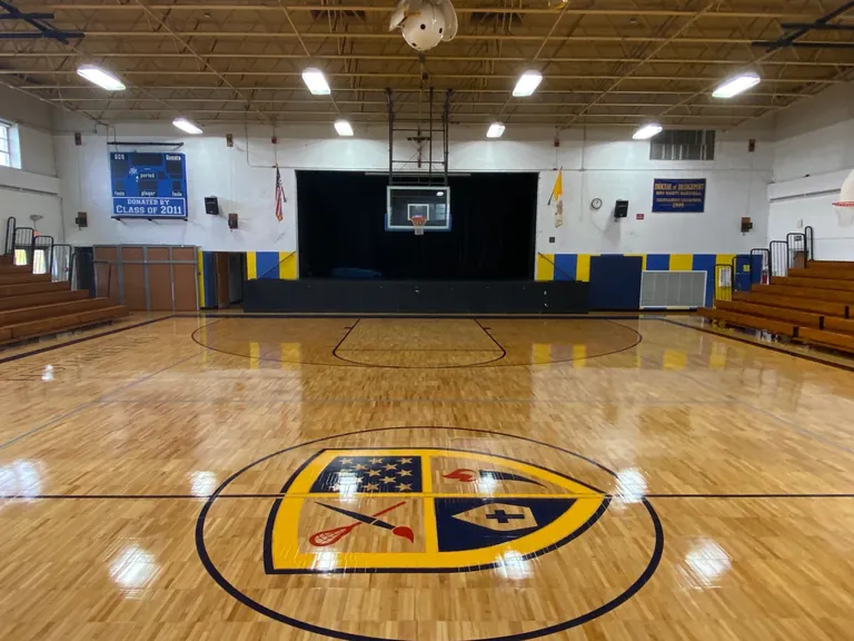 After: the same Greenwich Catholic School gym floor sanded and refinished by J and J, with bright maple, new game lines and the school crest at center court