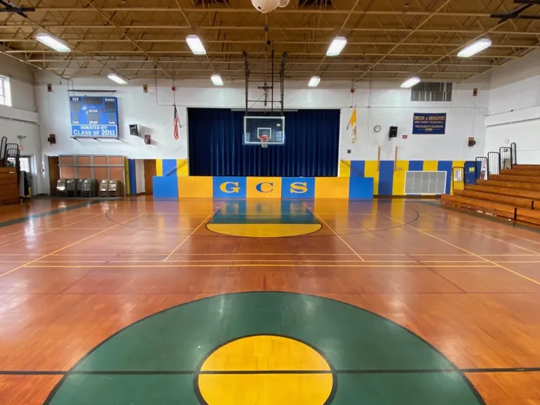 Before: Greenwich Catholic School gym floor with a worn, orange-toned finish, a green center circle and old lines