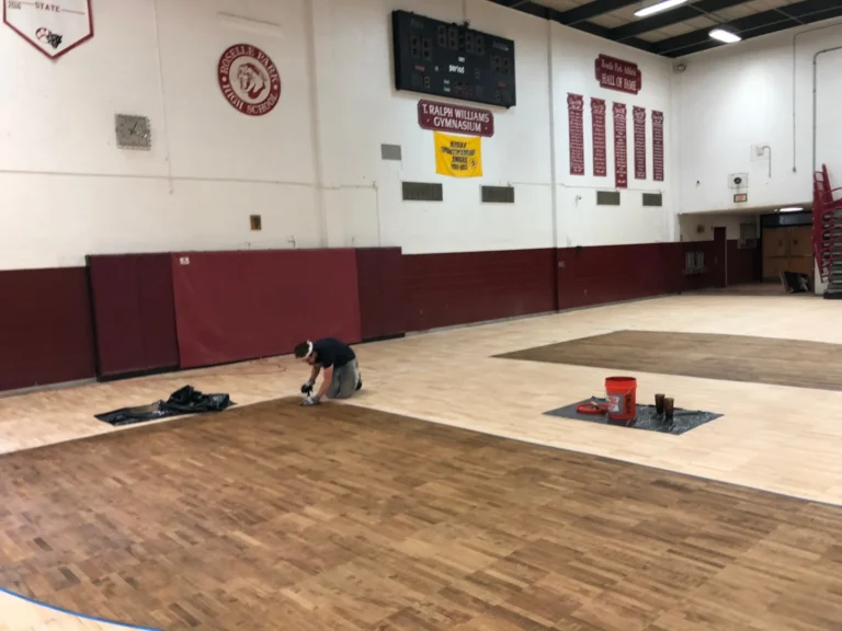 J and J worker applying finish during a full sand and refinish at T. Ralph Williams Gymnasium, Ocean Township, with maroon walls