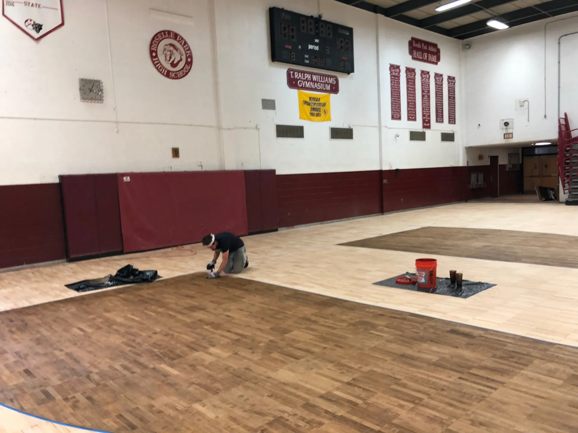 J and J worker applying finish during a full sand and refinish at T. Ralph Williams Gymnasium, Ocean Township, with maroon walls