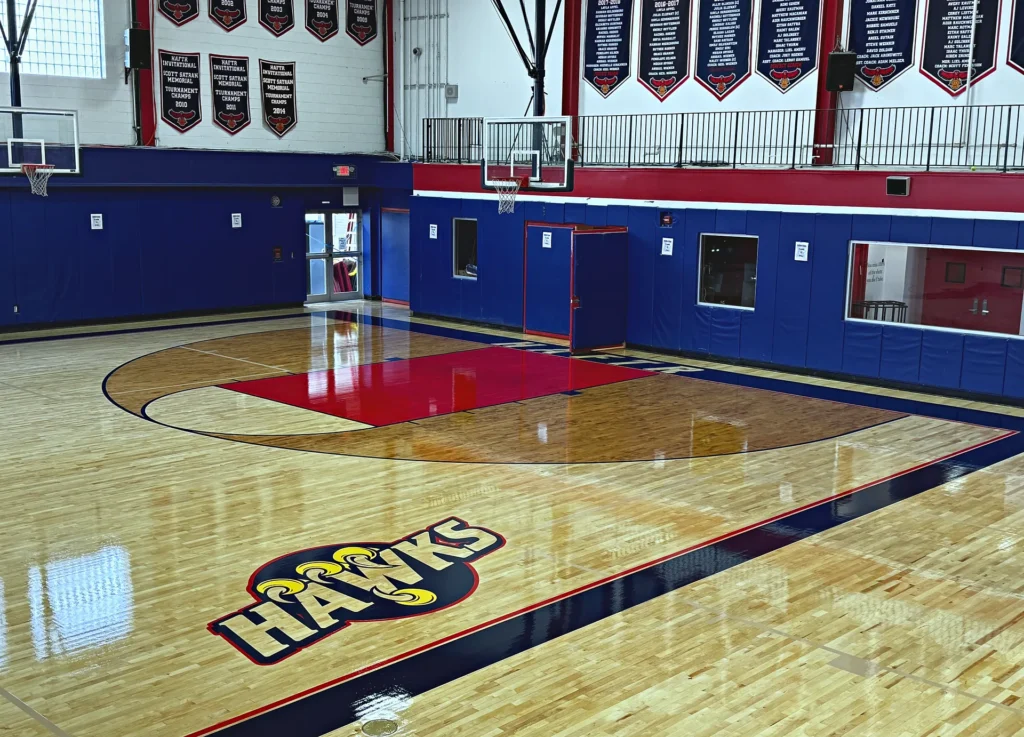 HAFTR Hawks logo painted on a refinished maple gym floor next to a red key and stained three-point arc