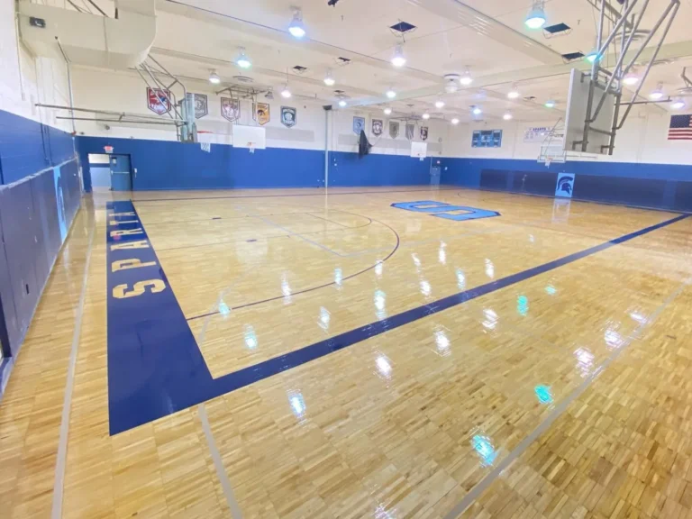 High-gloss maple gym floor with a blue painted key and navy border lettering