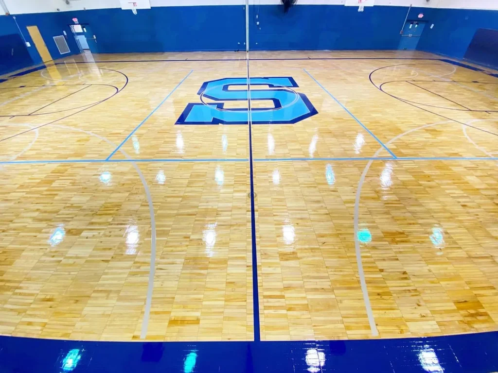 High-gloss finished maple gym floor with a light blue S center logo and navy game lines