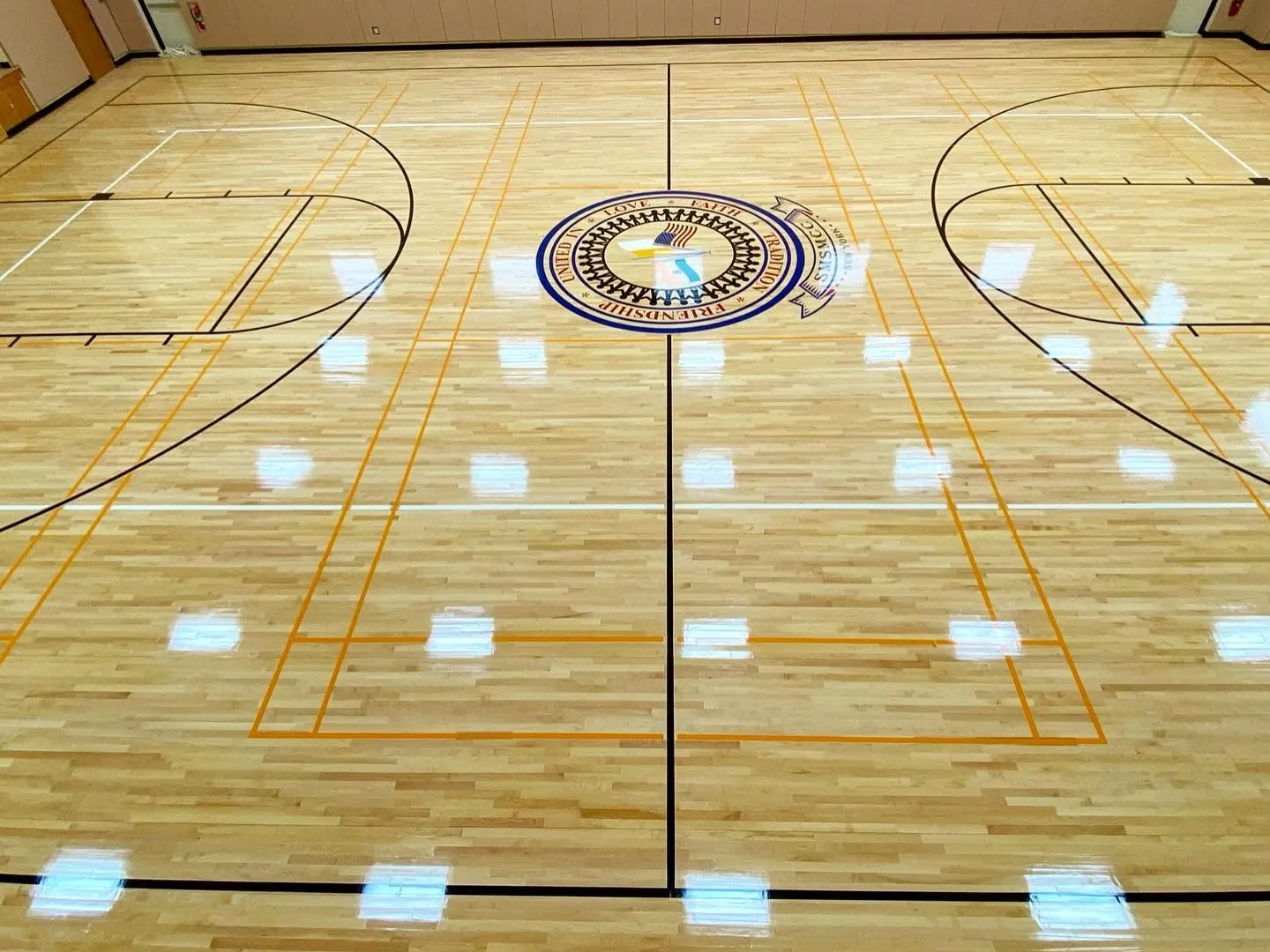 Glossy finished maple gym floor with a center seal and orange and black game lines