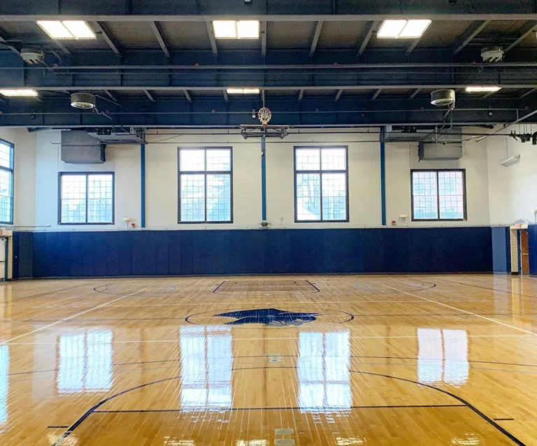 Bright, high-gloss finished maple gym floor with navy wall pads under tall windows
