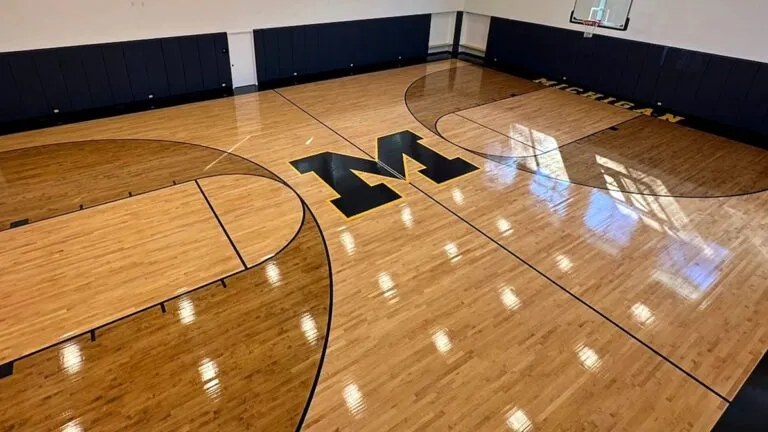 Home basketball court with glossy maple floor, block M logo and arched wood ceiling