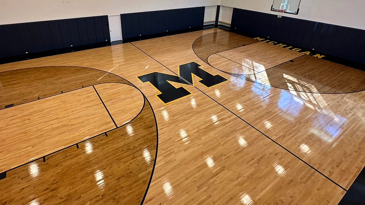 Home basketball court with glossy maple floor, block M logo and arched wood ceiling
