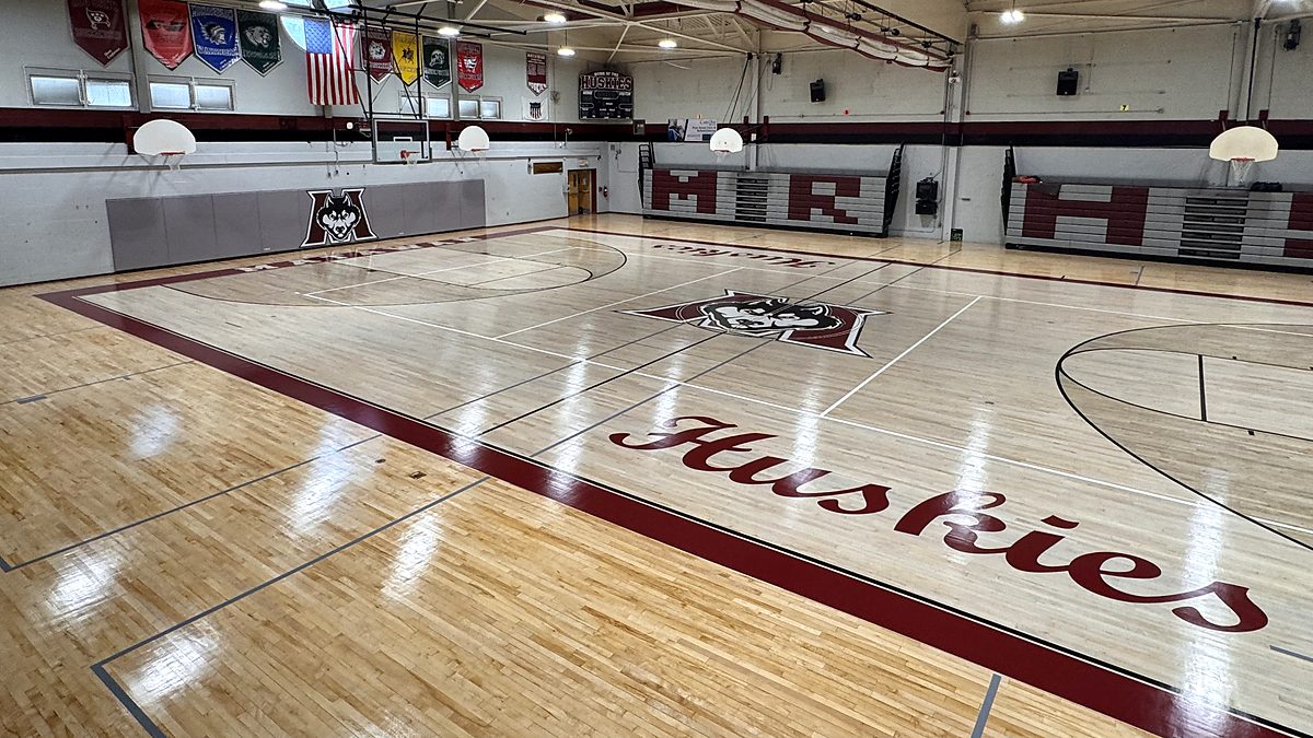 Glossy maple gym floor with maroon Huskies script, husky center logo and maroon border