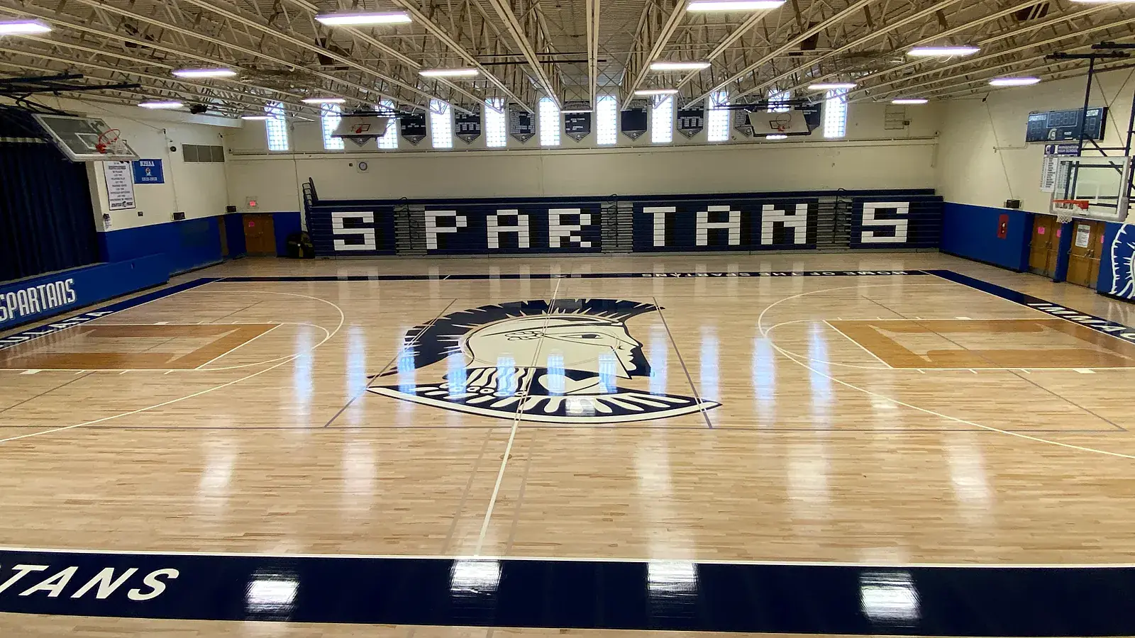 Overhead drone view of the Immaculata Spartans gym: glossy maple floor, Spartan center-court logo and SPARTANS lettering on the wall