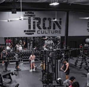 Large IRON CULTURE logo wall graphic above a busy weight room