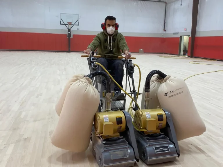 J and J technician running dual drum sanders with dust collection bags on a maple gym floor