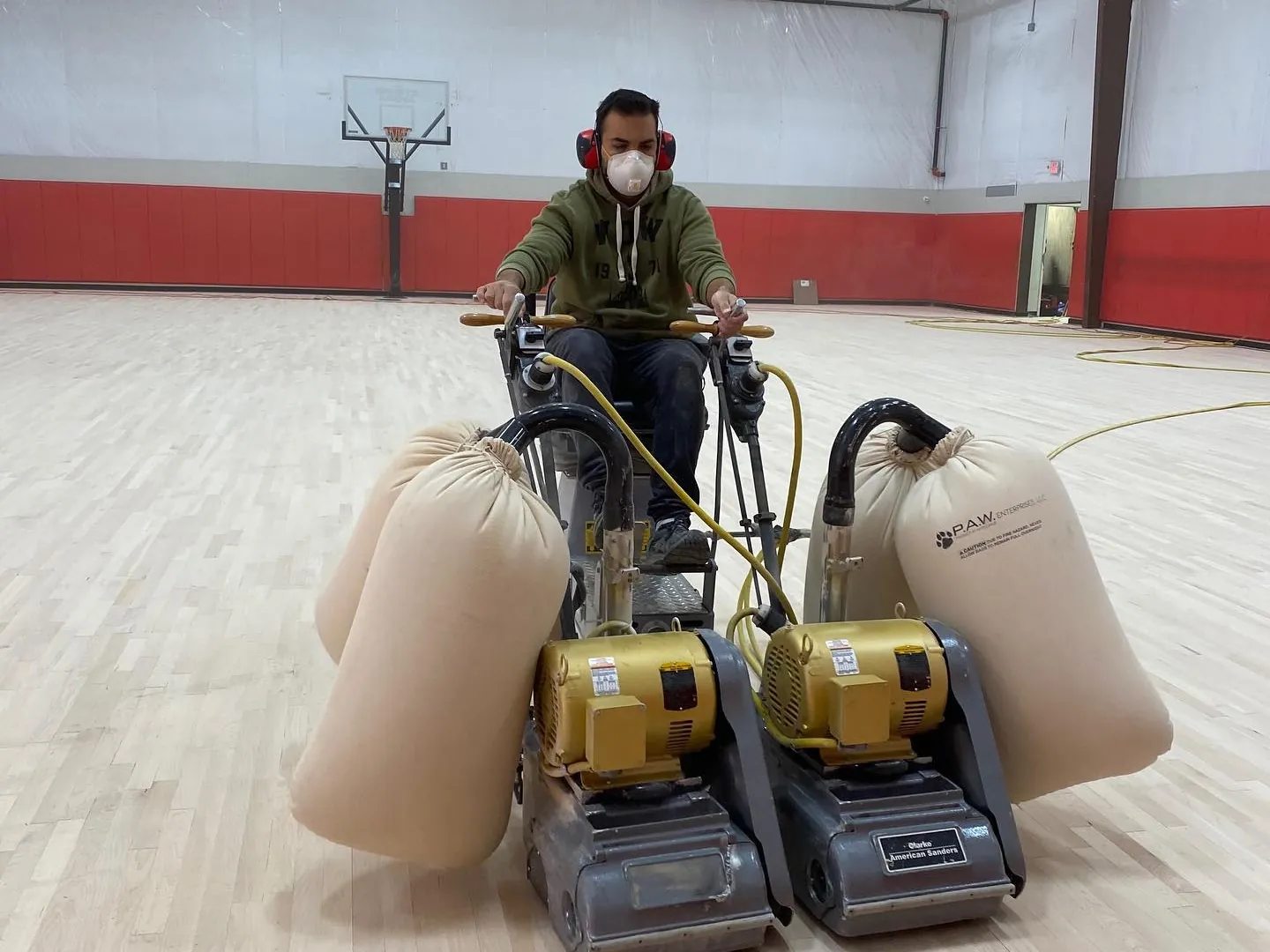 J and J technician running dual drum sanders with dust collection bags on a maple gym floor