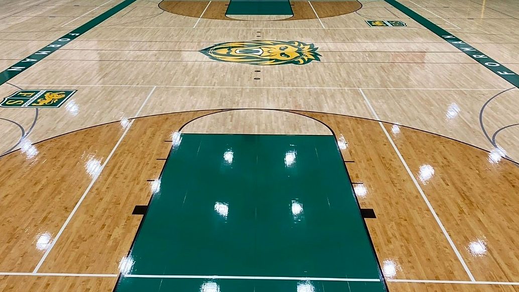 Glossy high school gym floor with green painted key and Lions center logo