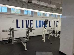 Blue LIVE LOVE LIFT lettering graphic on a white block wall in a school weight room