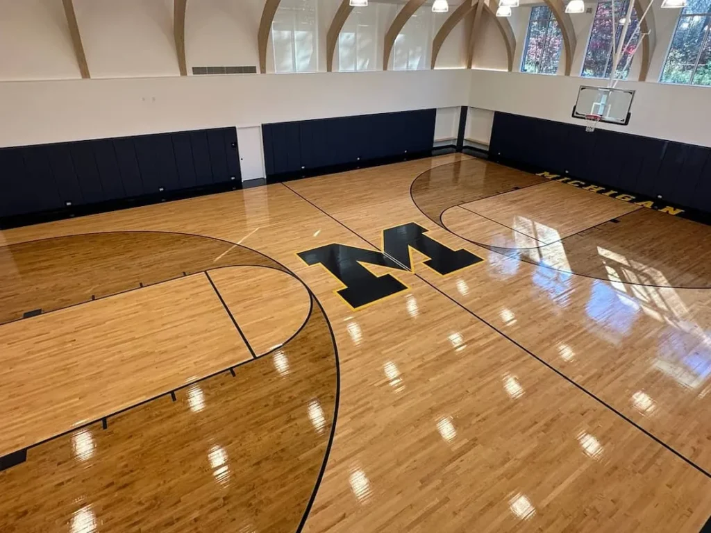 Glossy maple gym floor with a black M center logo and dark stained borders