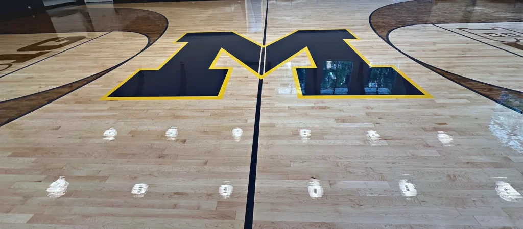 Private home gym with a high-gloss maple floor, navy and gold block letter logo and stained arcs