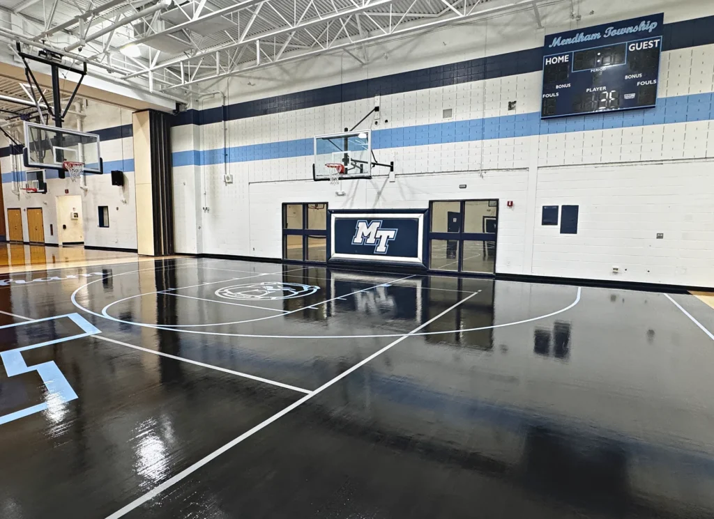 Mendham Township school gym with black-stained maple floor, light blue game lines and MT logo after a sand, stain and refinish by J and J Gym Floors