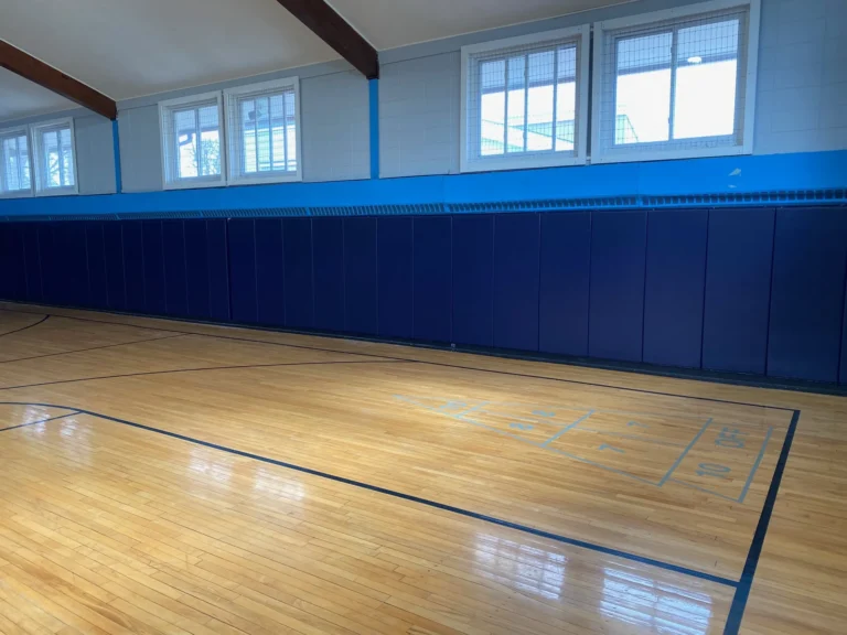 Long run of navy blue gym wall pads along a refinished maple gym floor