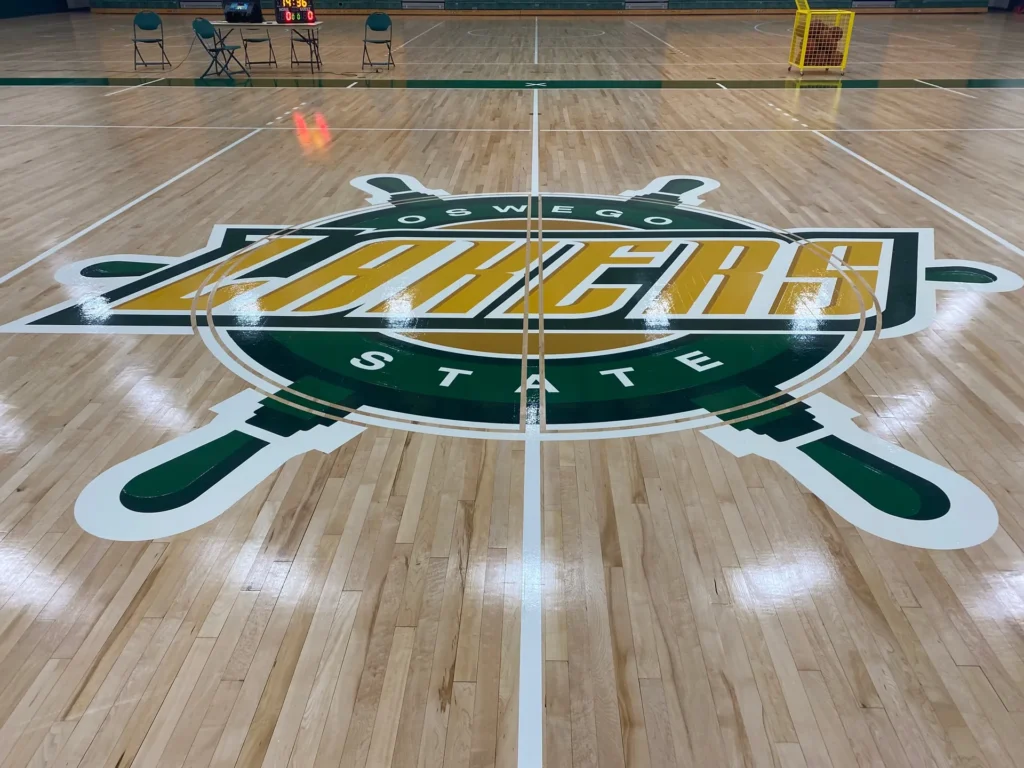 Oswego State Lakers green and gold center court logo painted on a maple gym floor