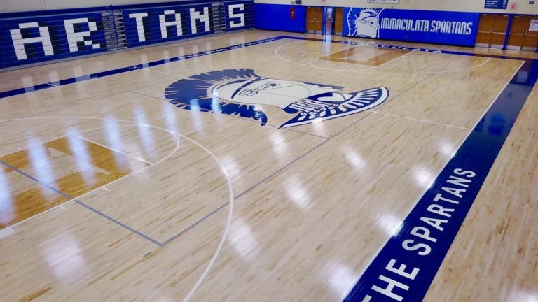 Glossy maple gym floor with a Spartans center court logo and sideline lettering