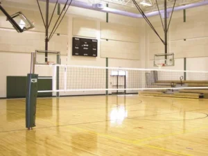 Volleyball net post with a green pad standing in a gym floor sleeve