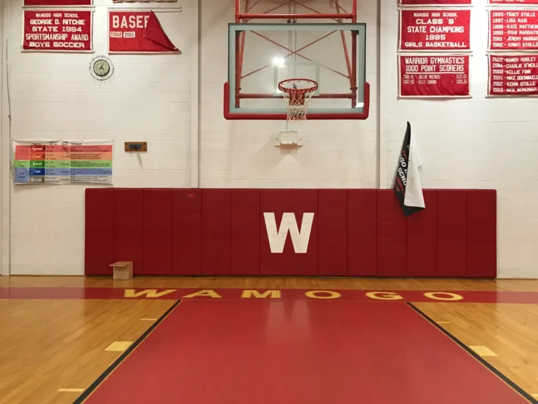 Red gym wall pad with the Wamogo W logo under a basketball hoop