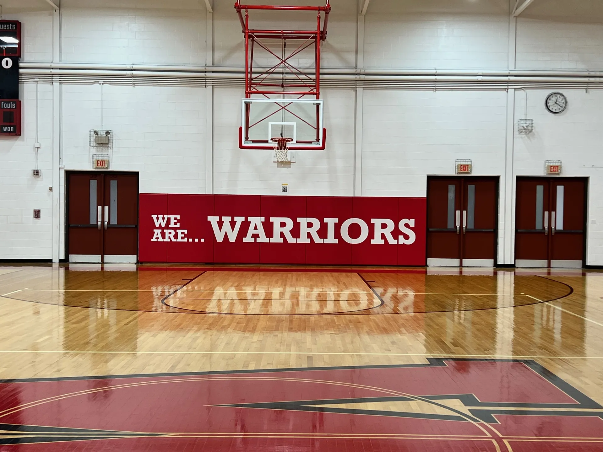 Red printed gym wall pad reading We Are Warriors under a basketball hoop